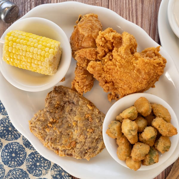 PoFolks fried chicken, country fried steak, fried okra, and corn on the cob on a white platter.
