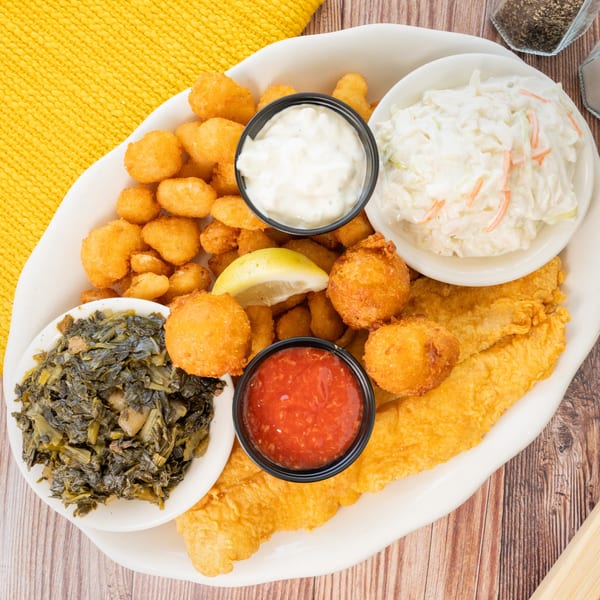 PoFolks fried fish platter with hushpuppies, popcorn shrimp, coleslaw, collard greens, and sauces.