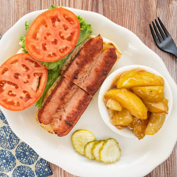 PoFolks' grilled hot dog with lettuce, tomato, a side of peaches, and pickles on a white plate.