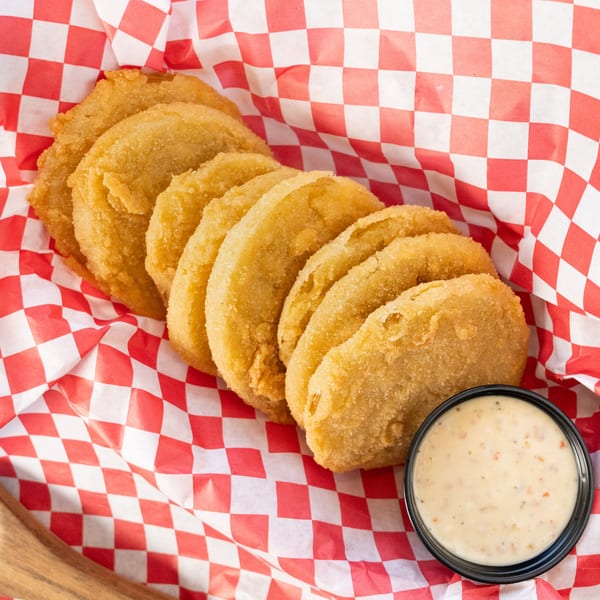 Golden-brown fried pickles in a red and white checkered basket with a side of dipping sauce.