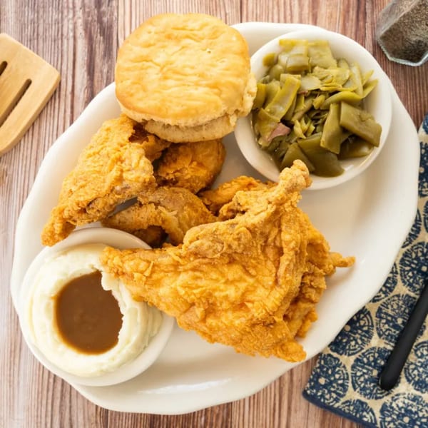 PoFolks fried chicken, mashed potatoes with gravy, green beans, and a biscuit on a white plate.